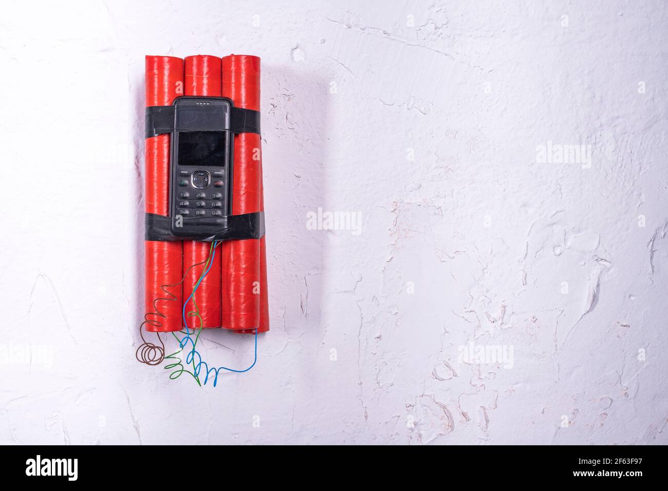 Dynamite with a remote fuse hung on a white wall. An explosive charge in an apartment building. Light background. Stock Photo