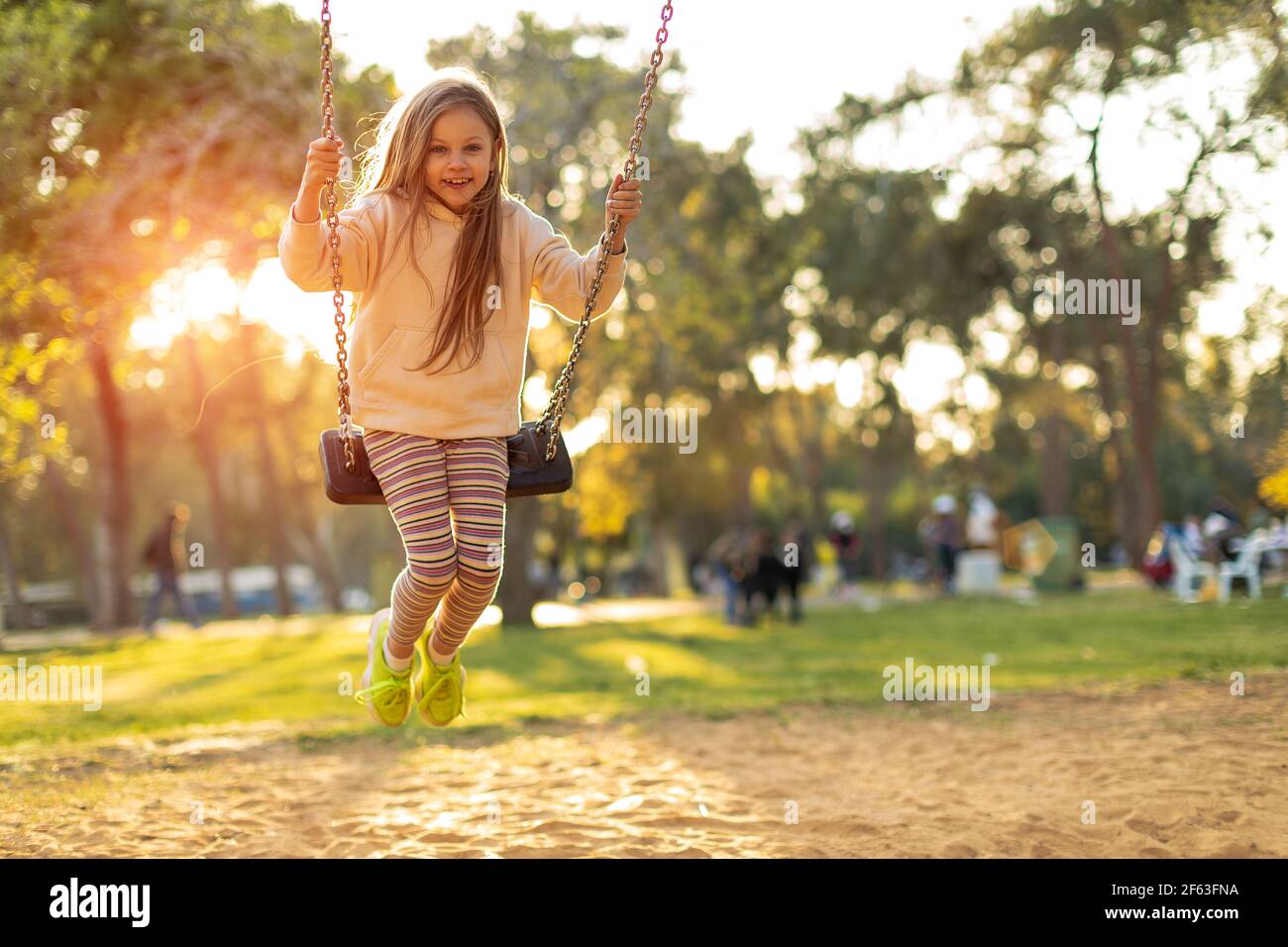 Girl holding chains of swings and swinging on a bright sunny day Stock Photo