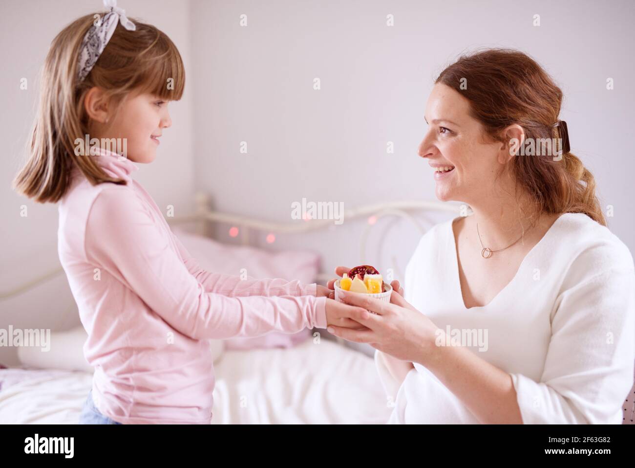 Close up of gorgeous pretty little toddler girl brings fruit salad to her excited mother. Stock Photo