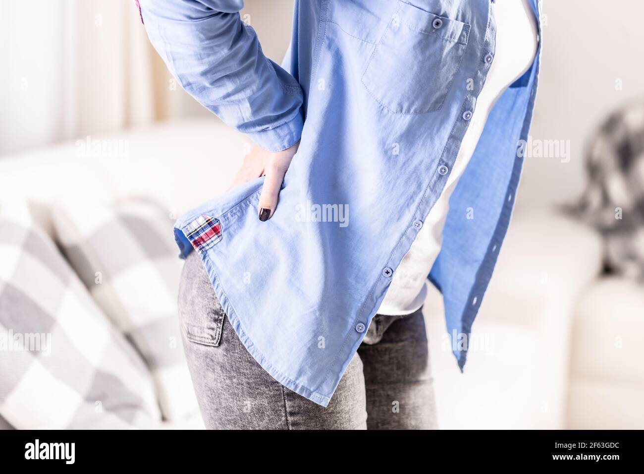 Detail of a woman sitting on a couch holding her lower back in pain