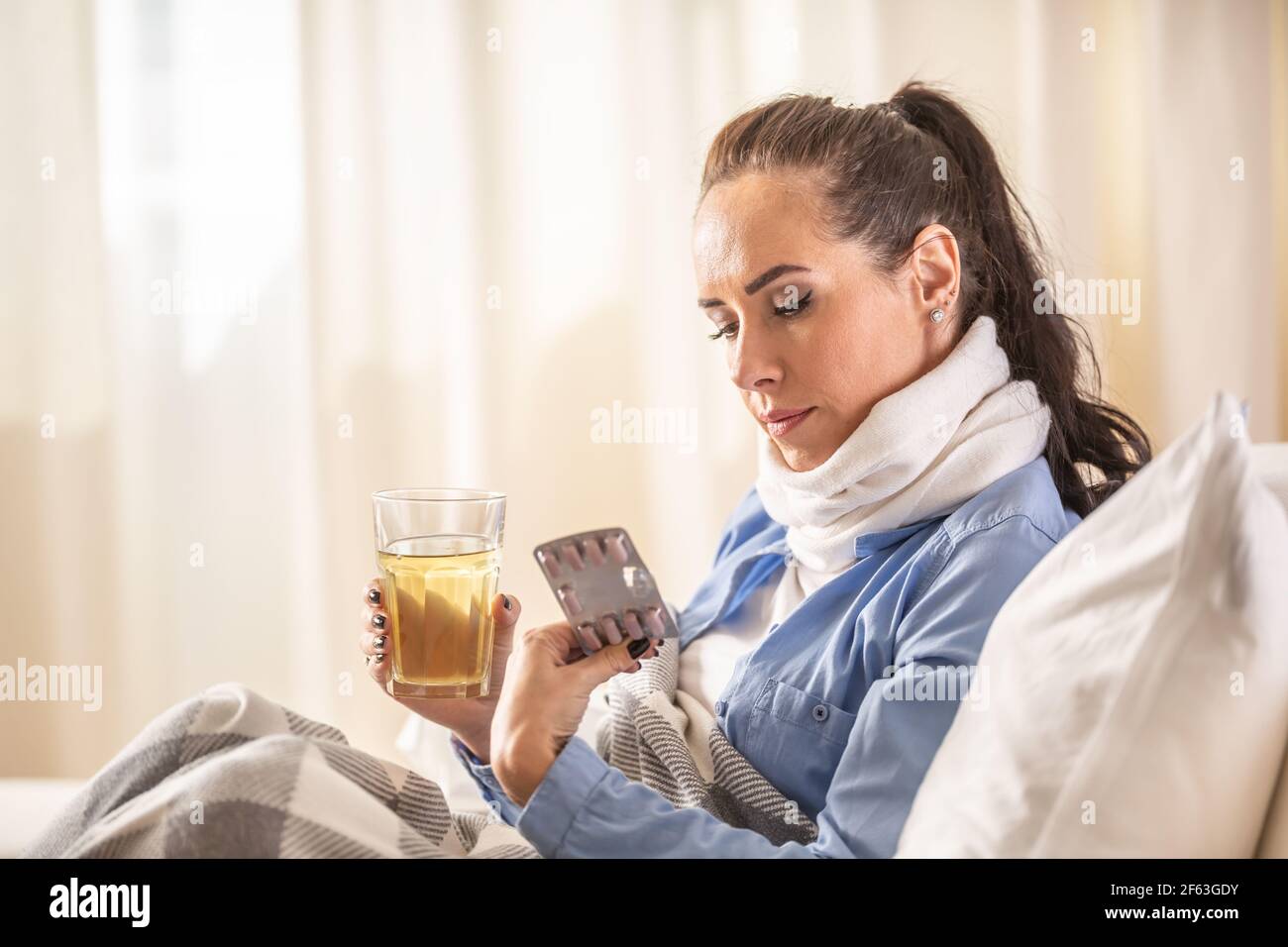 Woman in home treatment checks the blister pack of medicine holding hot tea cup in the other hand. Stock Photo