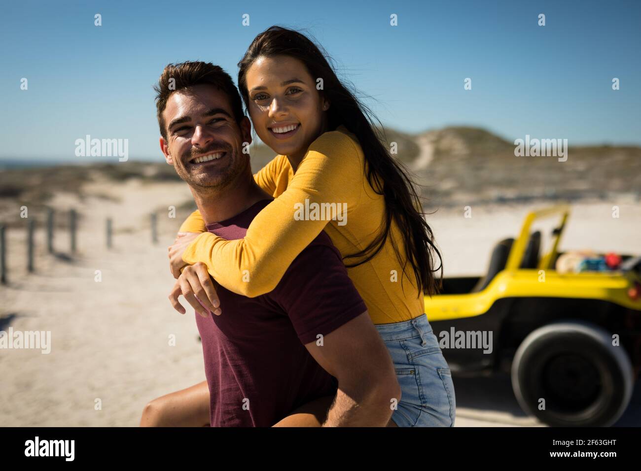 Happy caucasian couple next to beach buggy by the sea piggybacking Stock Photo