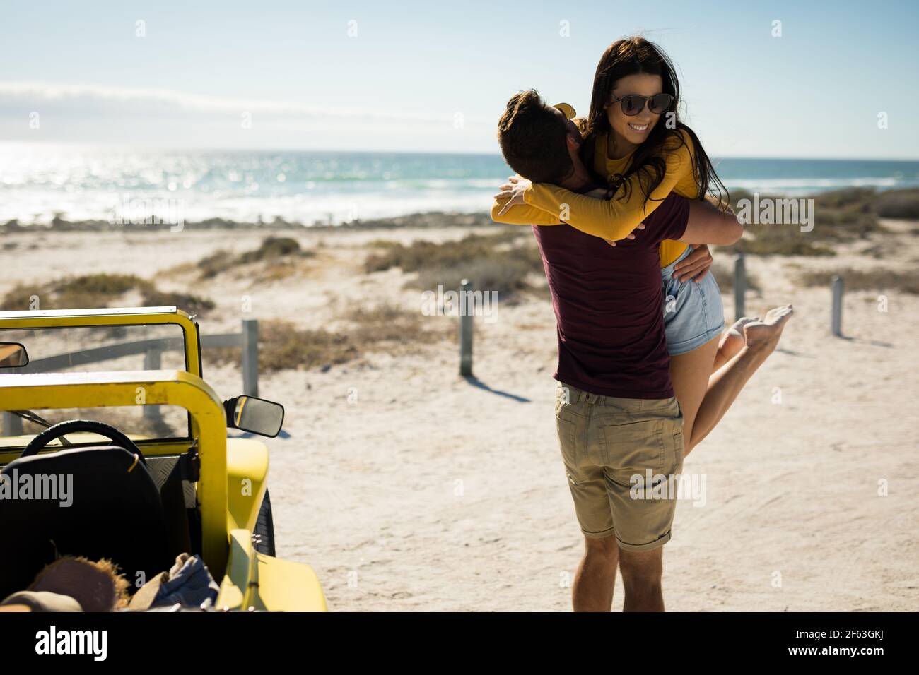 Happy caucasian couple staying next to beach buggy by the sea hugging Stock Photo