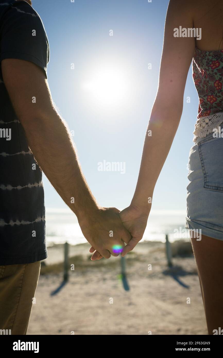 Midsection of caucasian couple on beach holiday holding hands Stock Photo
