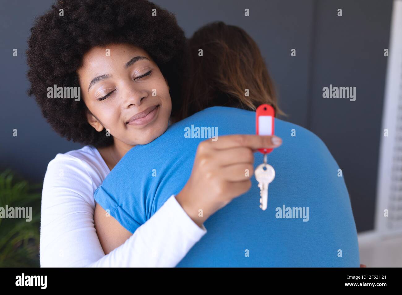 Happy diverse couple moving house smiling and embracing a woman holding key Stock Photo