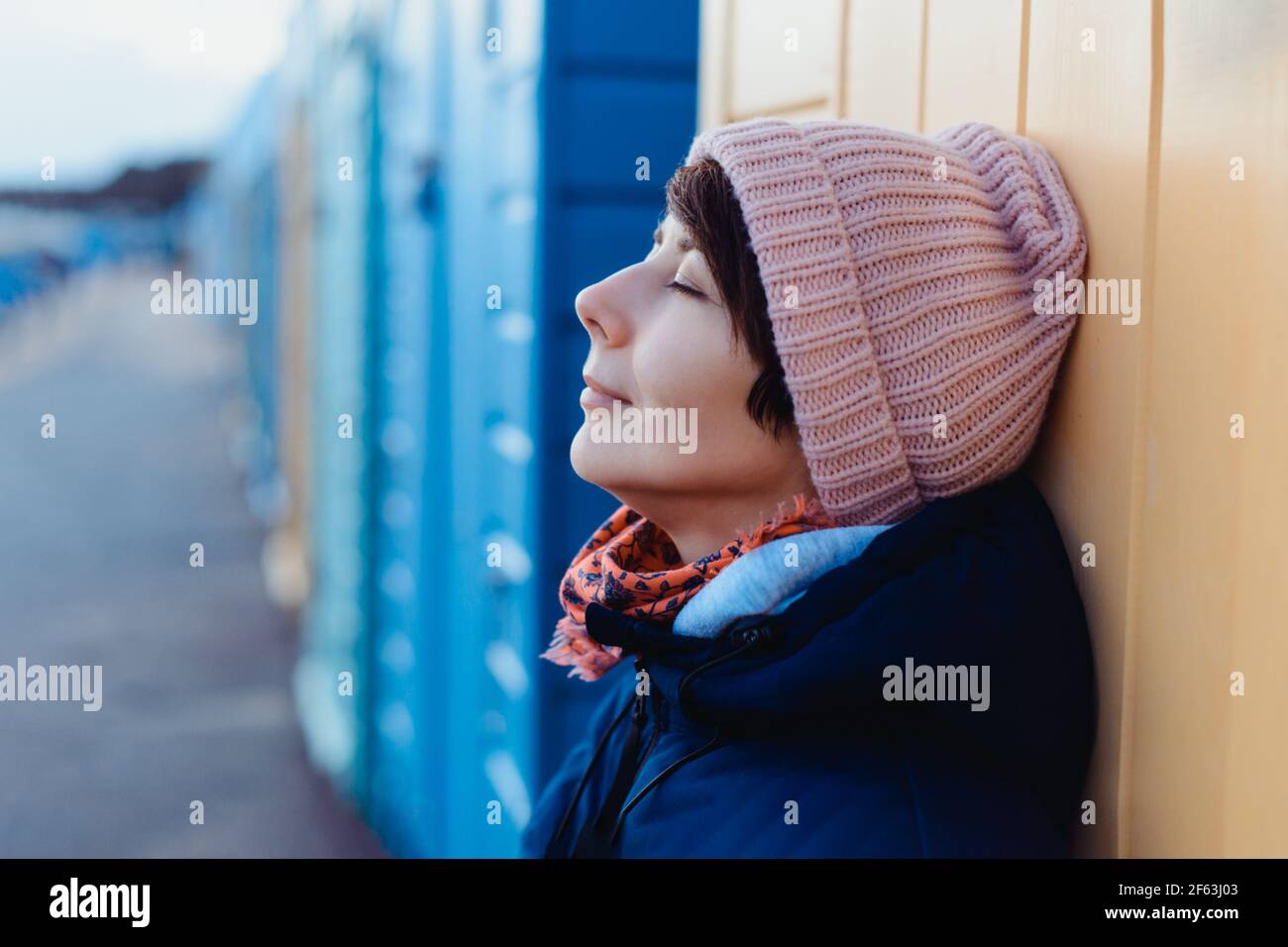 Close up smiling woman in warm clothes near colorful beach huts enjoying the moment during walk on the nature. Simple pleasures and personal Stock Photo