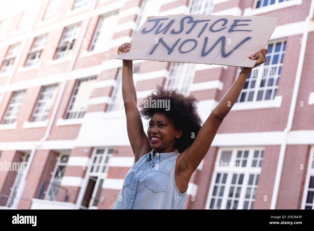 African american female protester on march holding a homemade protest sign above her head smiling Stock Photo