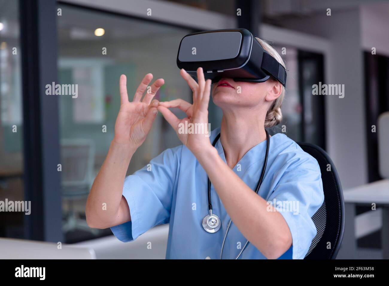 Caucasian female doctor wearing scrubs using vr headset and virtual interface Stock Photo