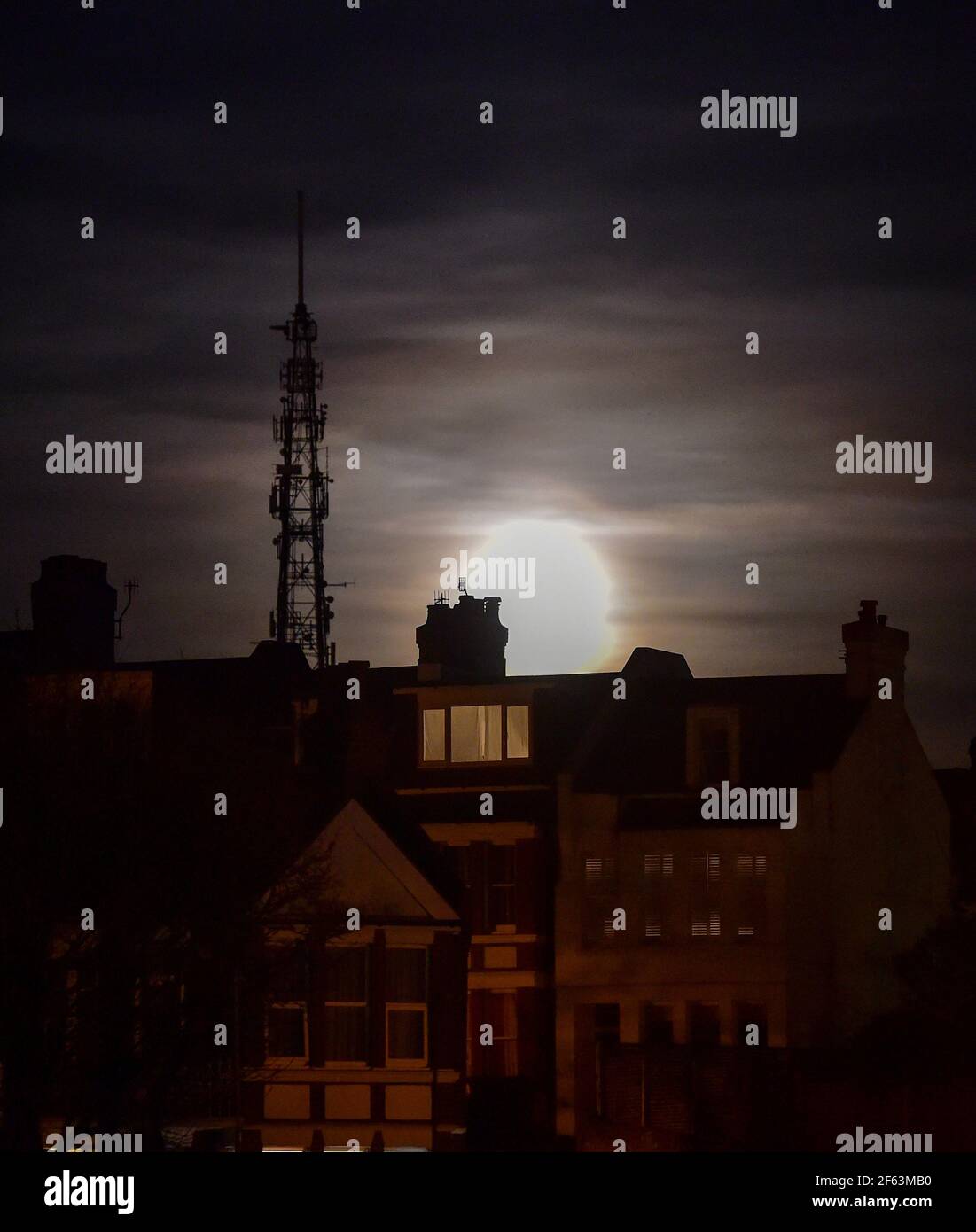 Brighton UK 29th March 2021 - The Worm Moon rises above houses in the Queens Park area of Brighton this evening . This will be the year's first supermoon, meaning the moon is slightly closer to Earth and therefore appears bigger and brighter in the sky. : Credit Simon Dack / Alamy Live News Stock Photo