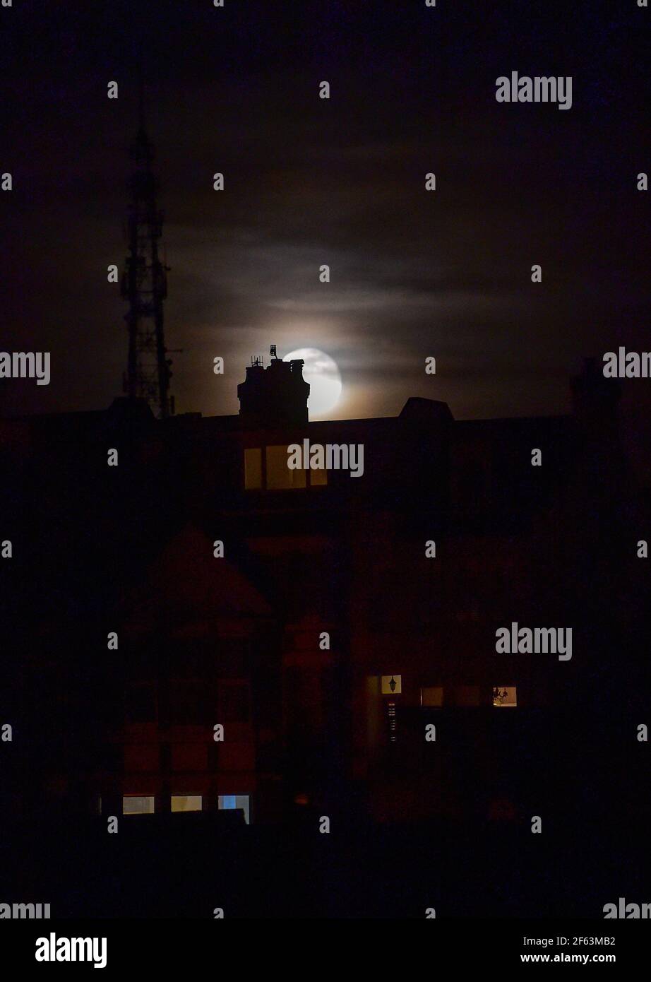 Brighton UK 29th March 2021 - The Worm Moon rises above houses in the Queens Park area of Brighton this evening . This will be the year's first supermoon, meaning the moon is slightly closer to Earth and therefore appears bigger and brighter in the sky. : Credit Simon Dack / Alamy Live News Stock Photo