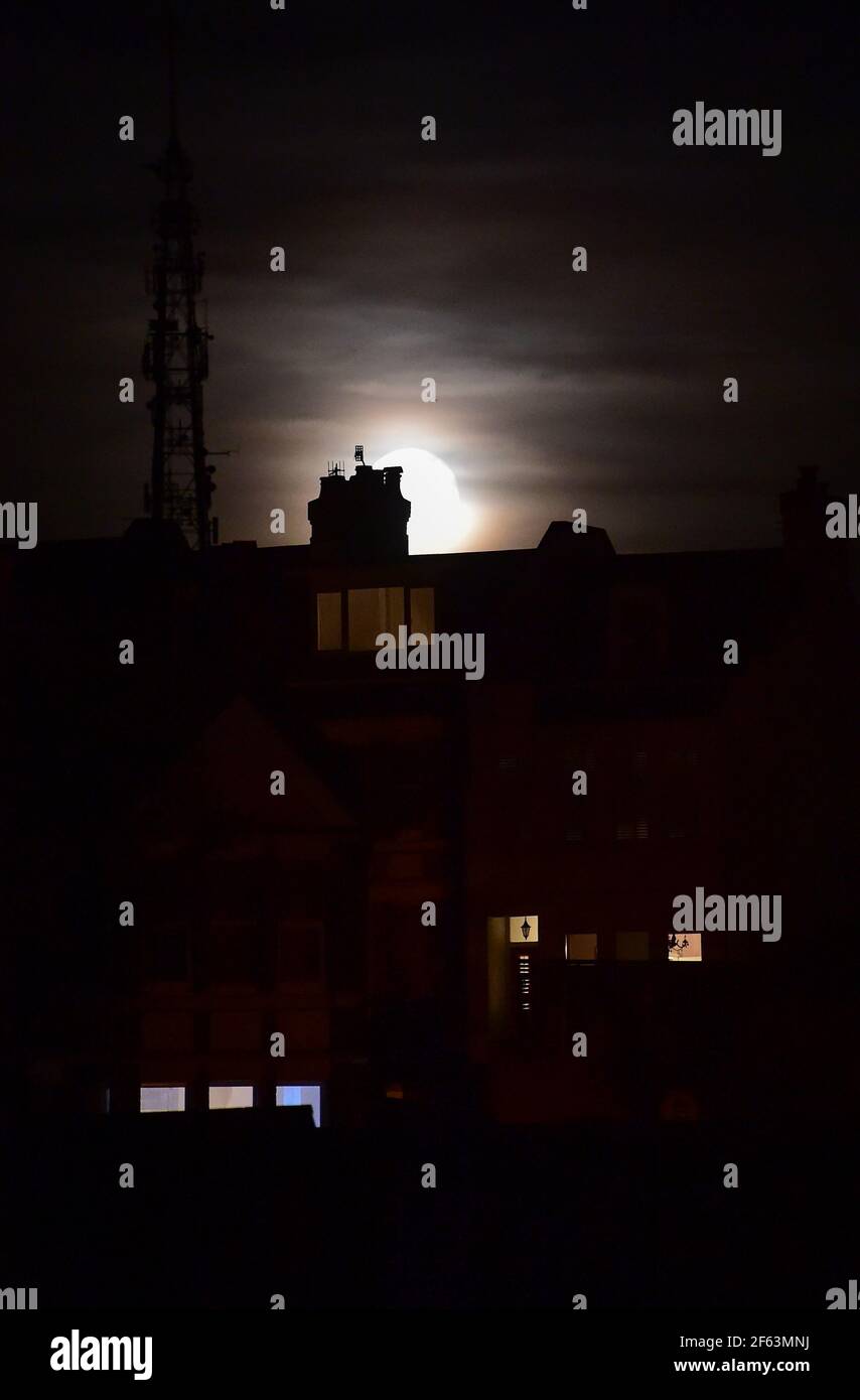 Brighton UK 29th March 2021 - The Worm Moon rises above houses in the Queens Park area of Brighton this evening . This will be the year's first supermoon, meaning the moon is slightly closer to Earth and therefore appears bigger and brighter in the sky. :  Credit Simon Dack / Alamy Live News Stock Photo