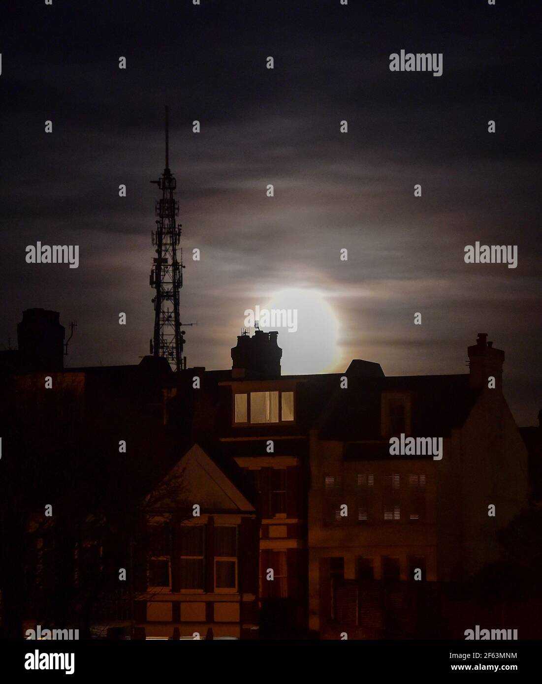 Brighton UK 29th March 2021 - The Worm Moon rises above houses in the Queens Park area of Brighton this evening . This will be the year's first supermoon, meaning the moon is slightly closer to Earth and therefore appears bigger and brighter in the sky. : Credit Simon Dack / Alamy Live News Stock Photo
