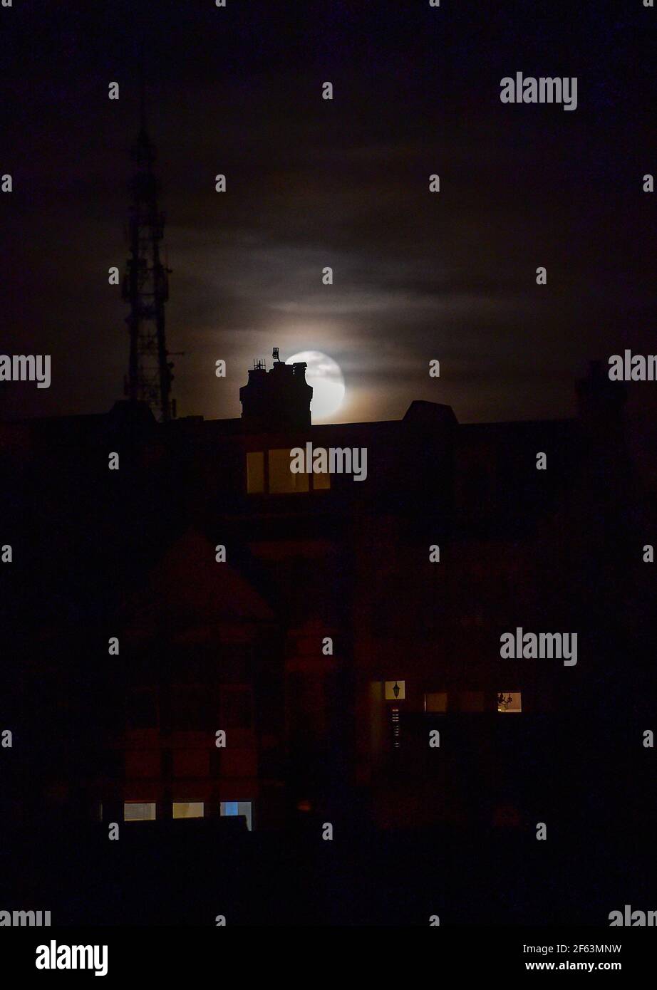 Brighton UK 29th March 2021 - The Worm Moon rises above houses in the Queens Park area of Brighton this evening . This will be the year's first supermoon, meaning the moon is slightly closer to Earth and therefore appears bigger and brighter in the sky. : Credit Simon Dack / Alamy Live News Stock Photo