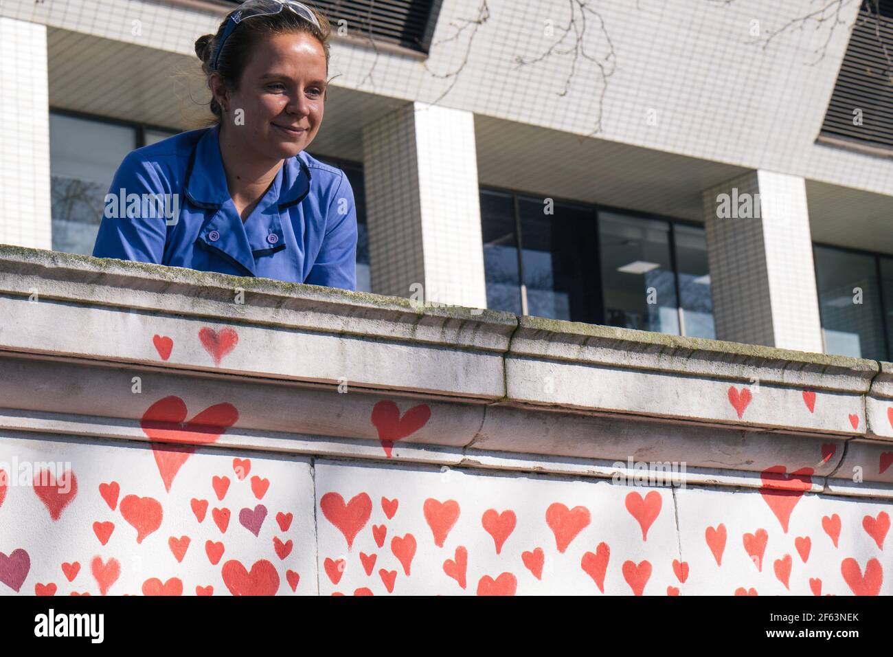 St Thomas's Hospital, London, UK. 29th March 2021. The bereaved and volunteers paint hearts for each person who has died of Covid. Medical staff from the hospital sit and look over the wall at the work. Credit: Denise Laura Baker/Alamy Live News Stock Photo