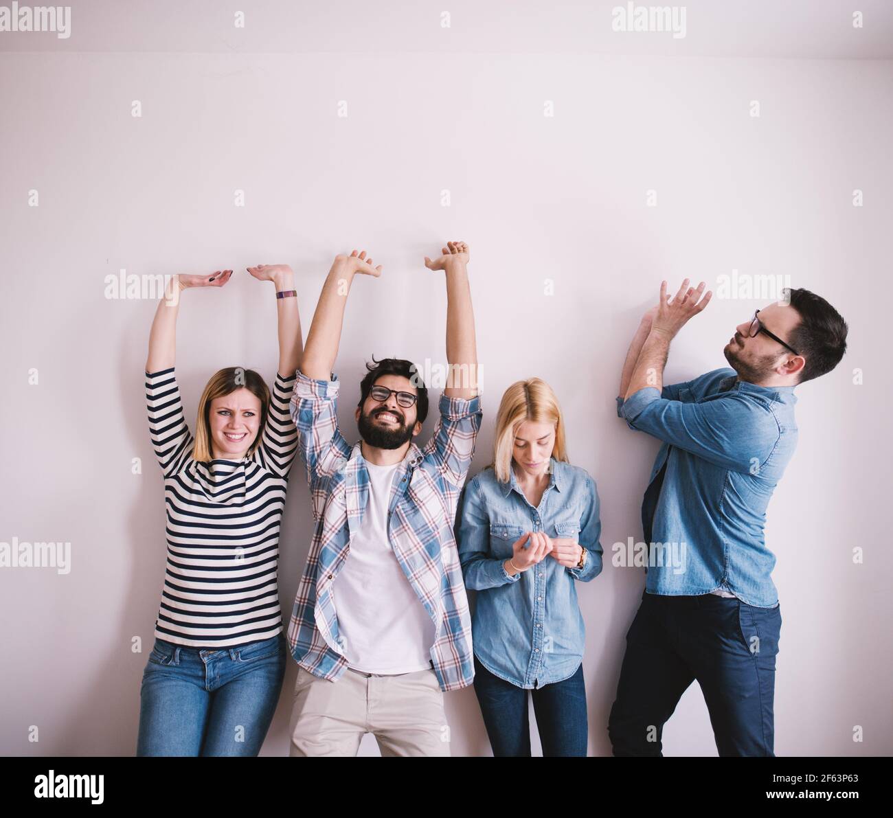 Group of young hardworking people leaning against the wall like raising something while one of them looking at nails. Stock Photo
