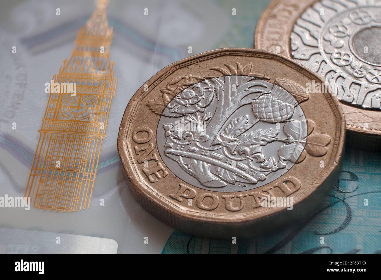 British one pound coin placed on top of polymer 5 Pound banknote with visible Big Ben symbol. Concept. Selective focus. Macro. Stock Photo