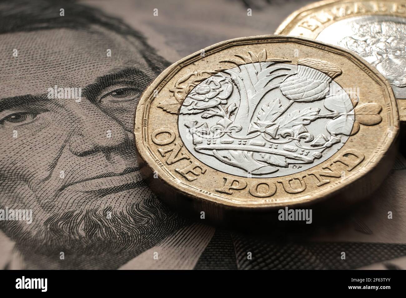 British one pound coin placed on top of US 5 dollar banknote with Lincoln face. Concept. Selective focus. Macro. Stock Photo