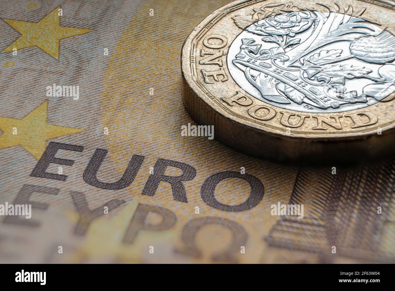 British one pound coin placed on top of 50 EURO banknote with visible words 'EURO' translated in different languages. Concept. Selective focus. Macro. Stock Photo