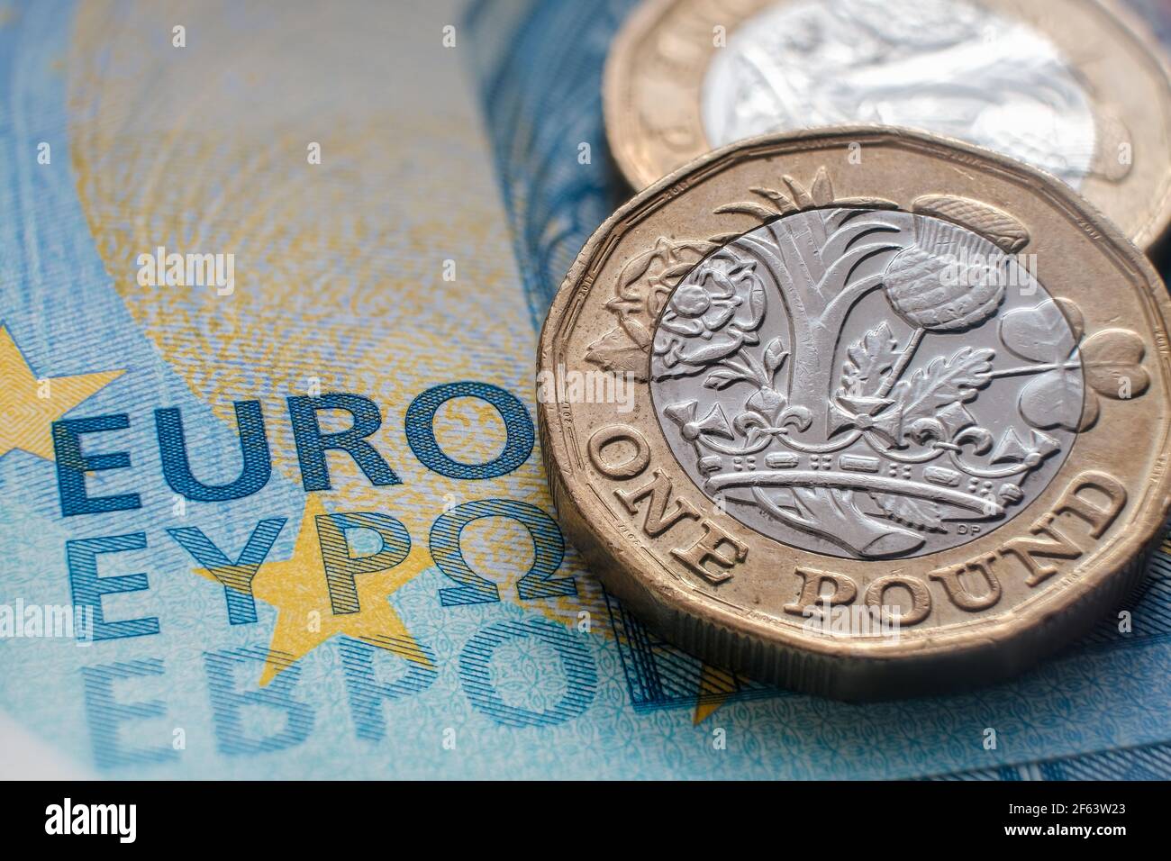 British one pound coin placed on top of 20 EURO banknote with visible words 'EURO' translated in different languages. Concept. Selective focus. Macro. Stock Photo