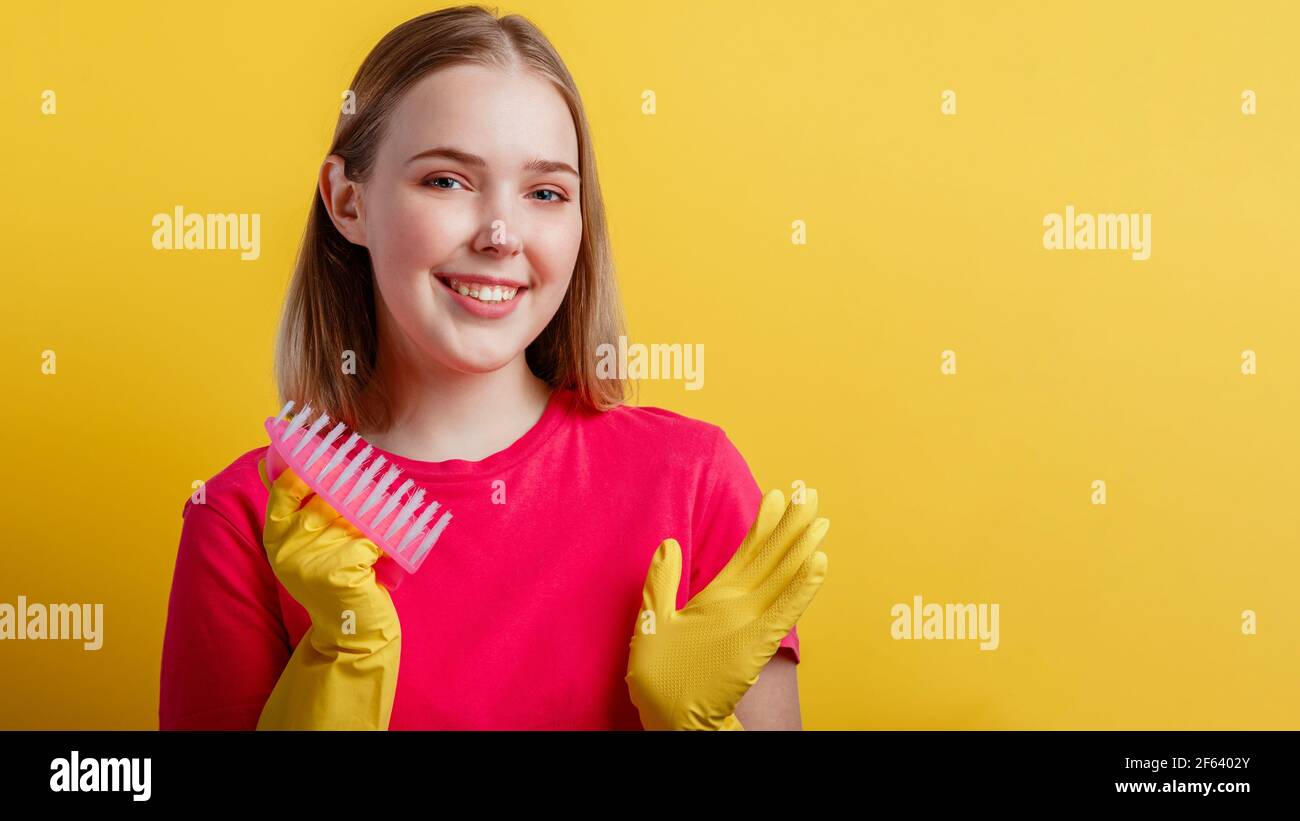 Woman Portrait with cleaning brush in rubber gloves. Young blonde happy smiling woman ready to cleaning house with household supplies isolated over ye Stock Photo