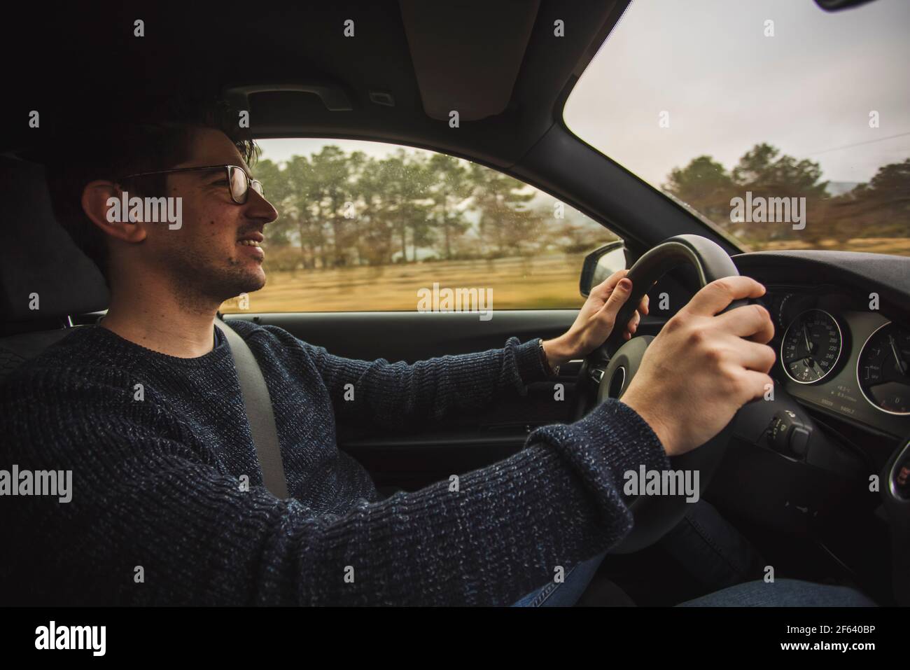 Happy guy sitting driving a car with two hands on the steering wheel Stock Photo