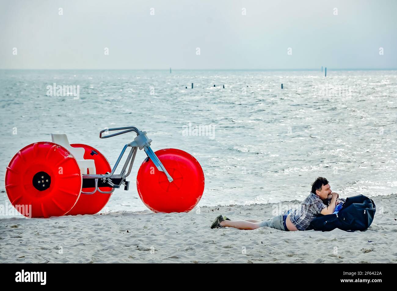 A man lays in the sand beside a beach buggy and watches people on Biloxi Beach, March 27, 2021, in Biloxi, Mississippi. Stock Photo
