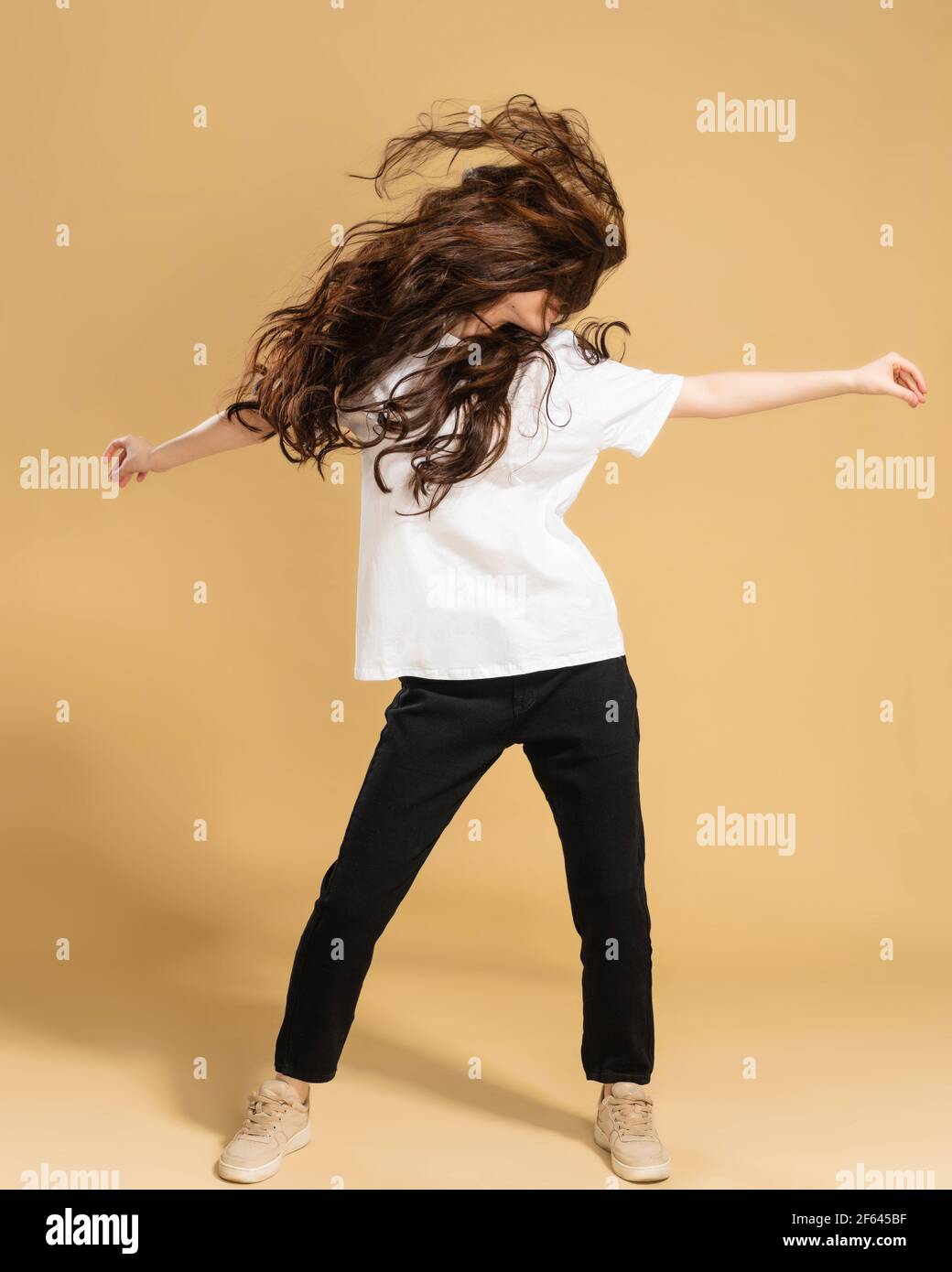 Young slender girl in a white t-shirt dancing and waving long hair on a pastel orange studio background. Stock Photo