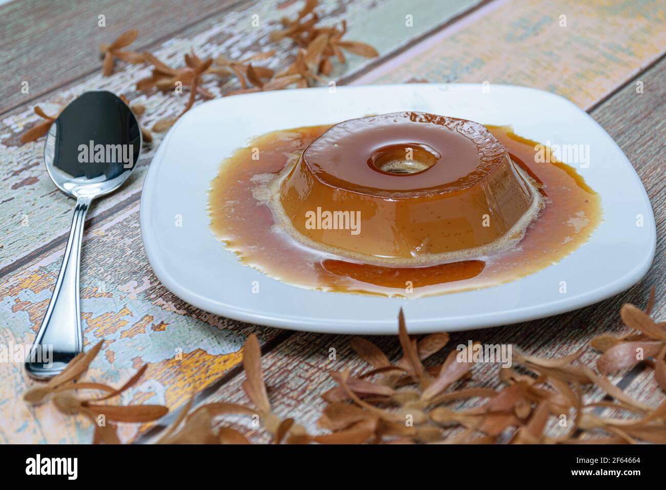 Dulce de leche pudding with caramel sauce, next to a spoon and flying seeds (Triplaris americana). A traditional Brazilian sweet. Stock Photo
