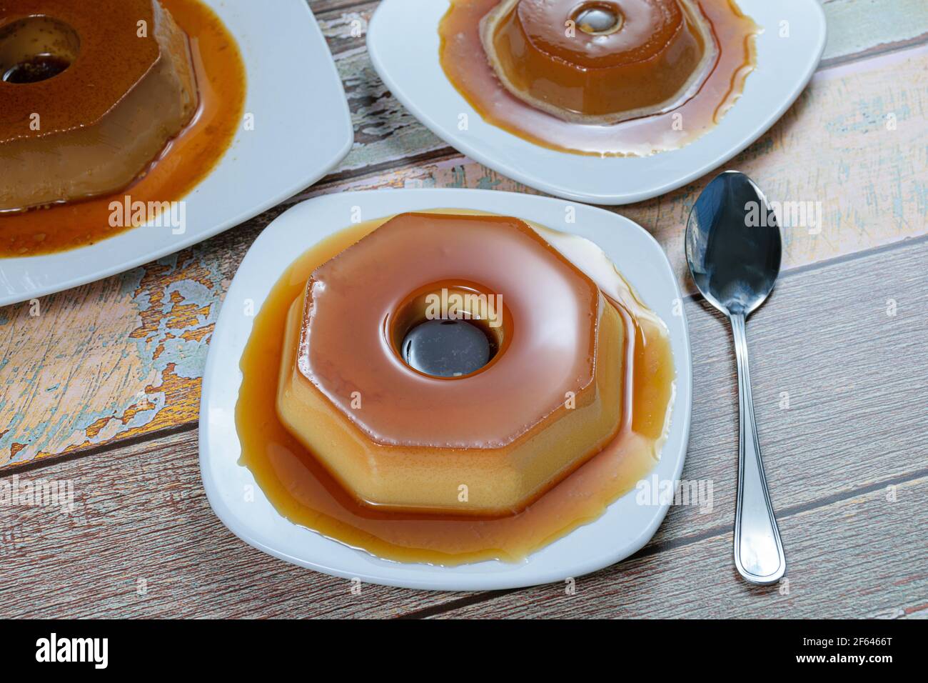 Condensed milk pudding with caramel syrup, surrounded by other puddings and a spoon. Traditional Brazilian sweet. Stock Photo