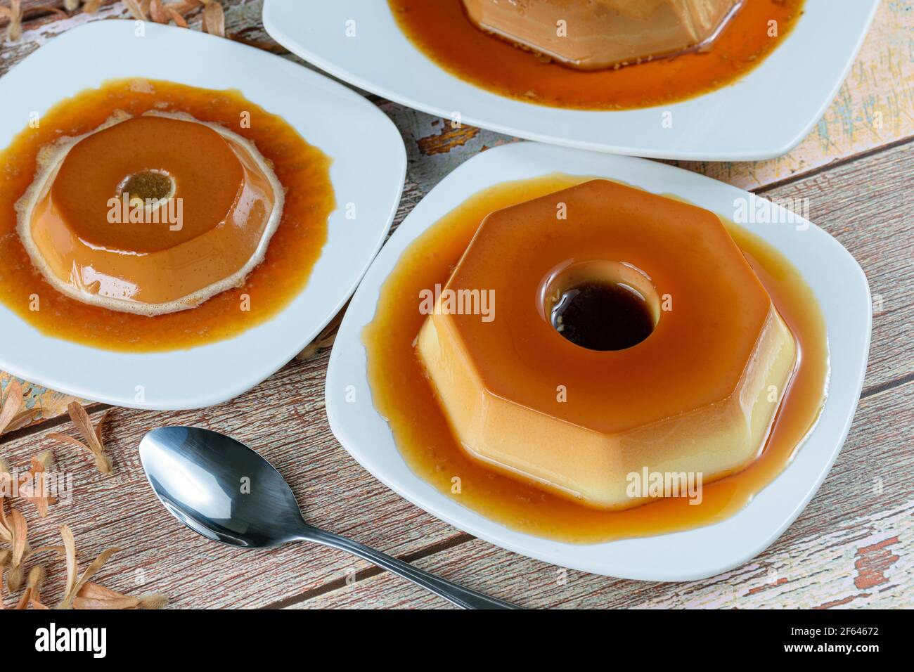 Condensed milk pudding with caramel syrup, surrounded by other puddings, spoon and flying seeds (Triplaris amaricana). Traditional Brazilian sweet. Stock Photo