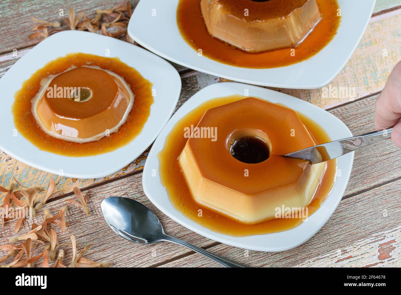 Man cutting a condensed milk pudding with caramel syrup, surrounded by other puddings, spoon and flying seeds (Triplaris amaricana). Traditional Brazi Stock Photo