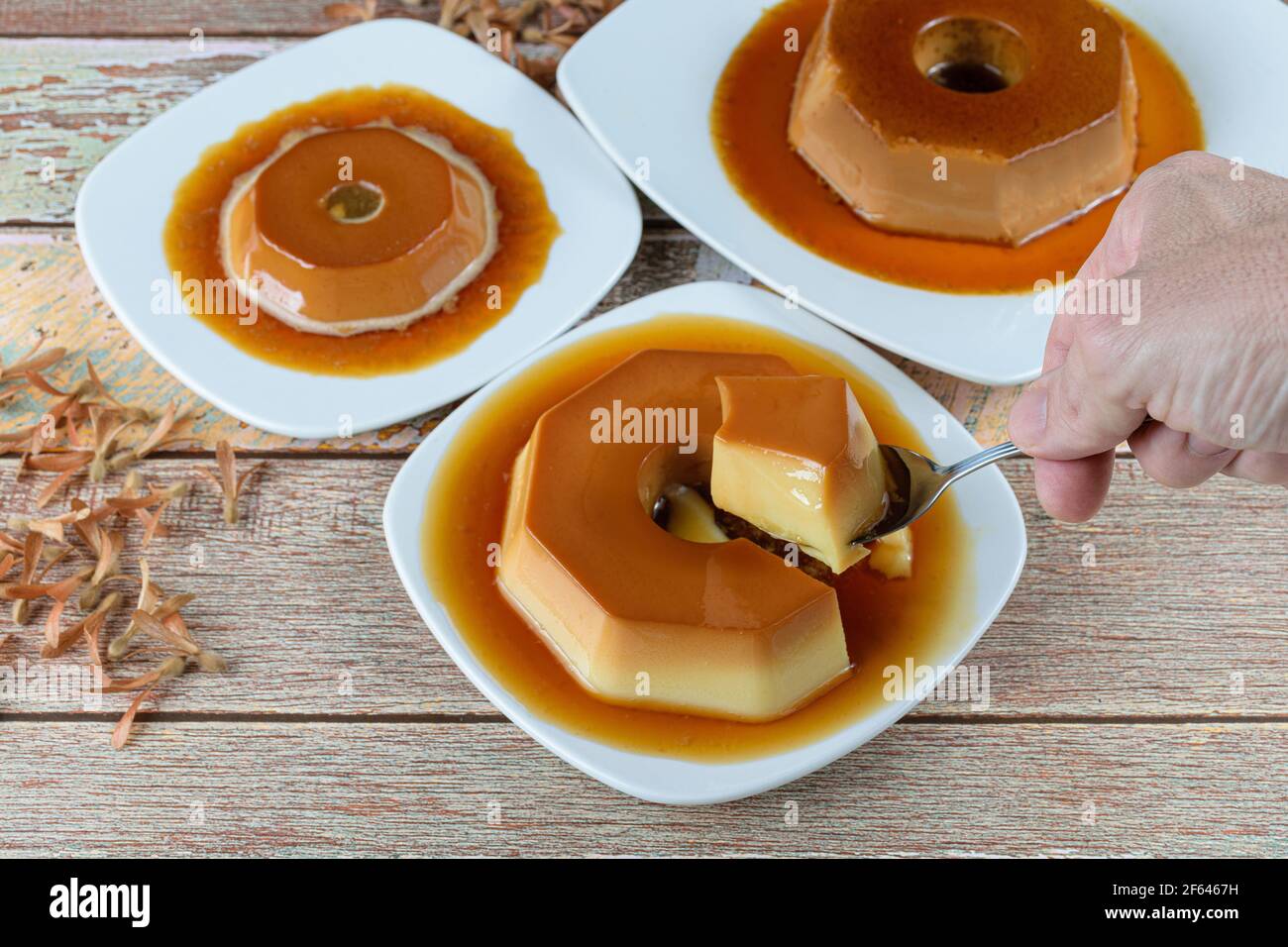 Man taking a slice with a spoon of condensed milk pudding with caramel sauce, alongside other puddings and flying seeds (Triplaris amaricana). Traditi Stock Photo