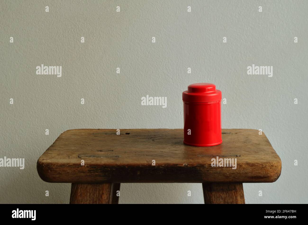 Closed lid red metal box standing on vintage wooden chair against white cement wall Stock Photo