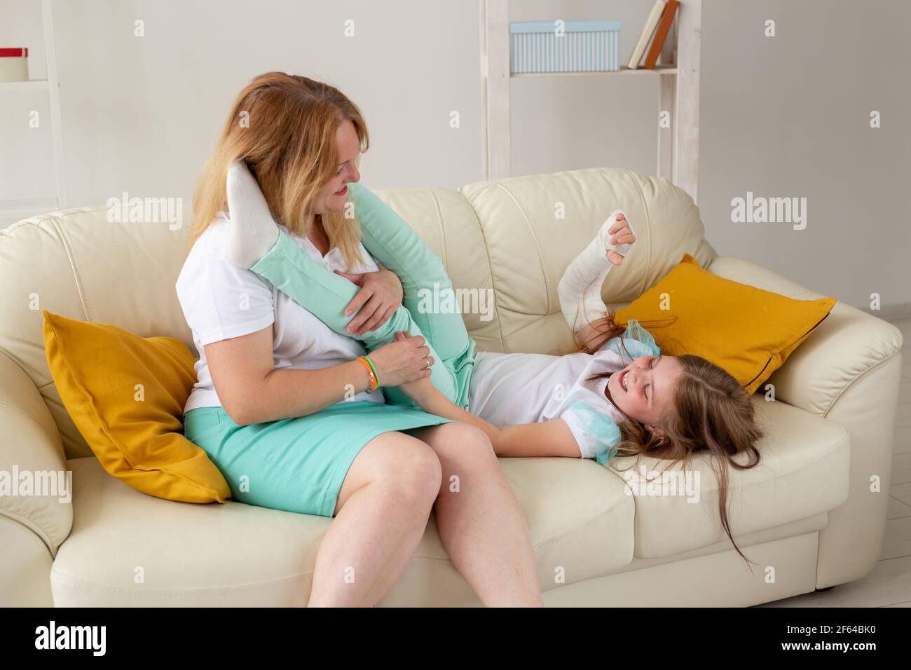 Child with broken arm and gypsum spend time at home with mother. Childhood illnesses, a positive outlook and recovery. Stock Photo