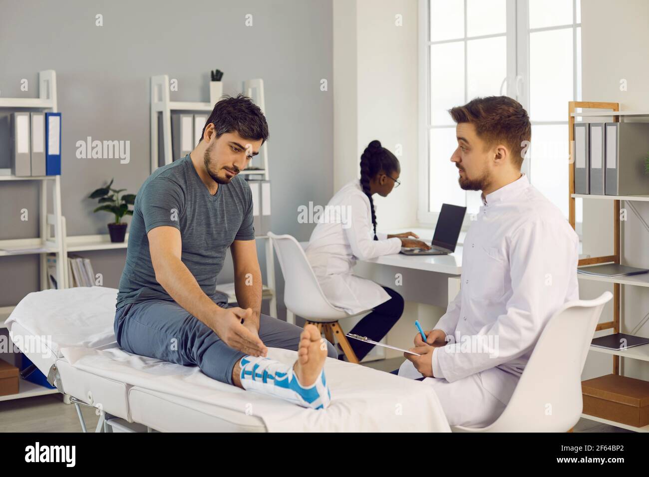 Male doctor and man patient during check-up for leg injury in hospital ward Stock Photo