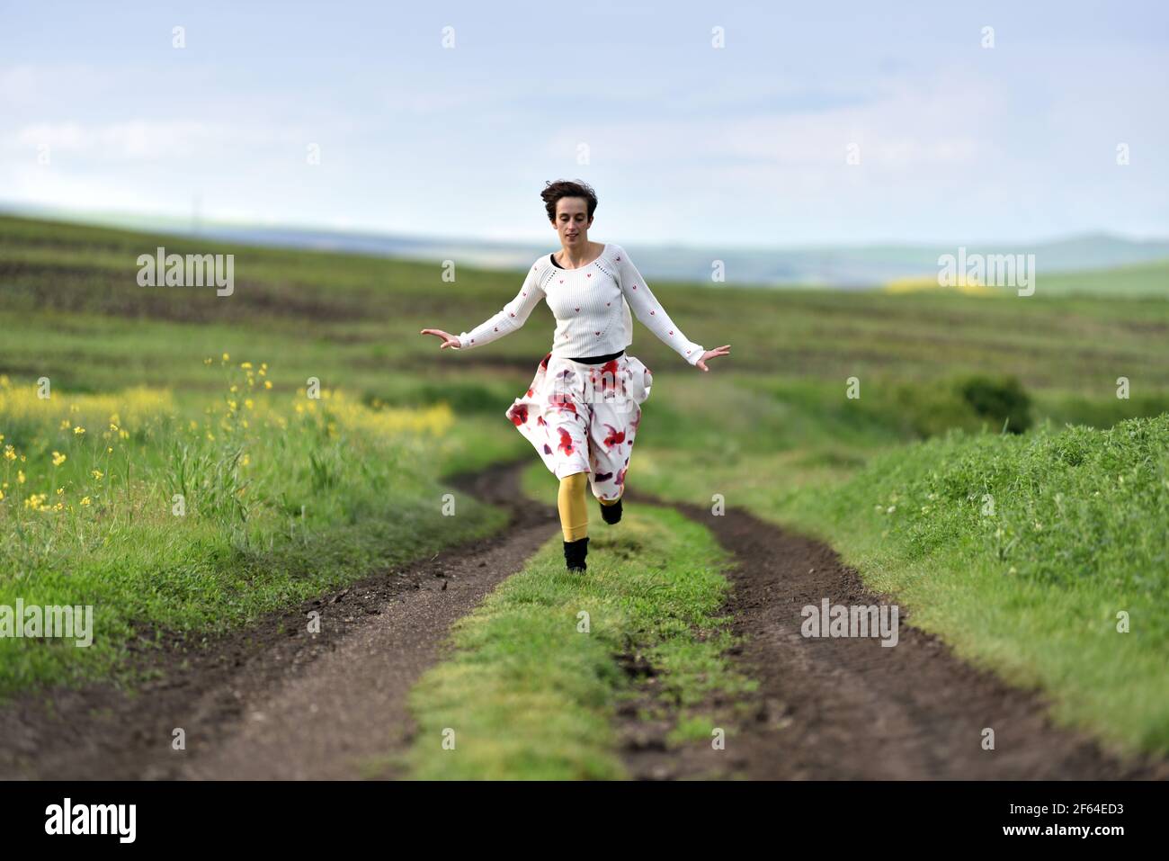 Joyful younf woman in skirt running in canola field in the spring Stock Photo