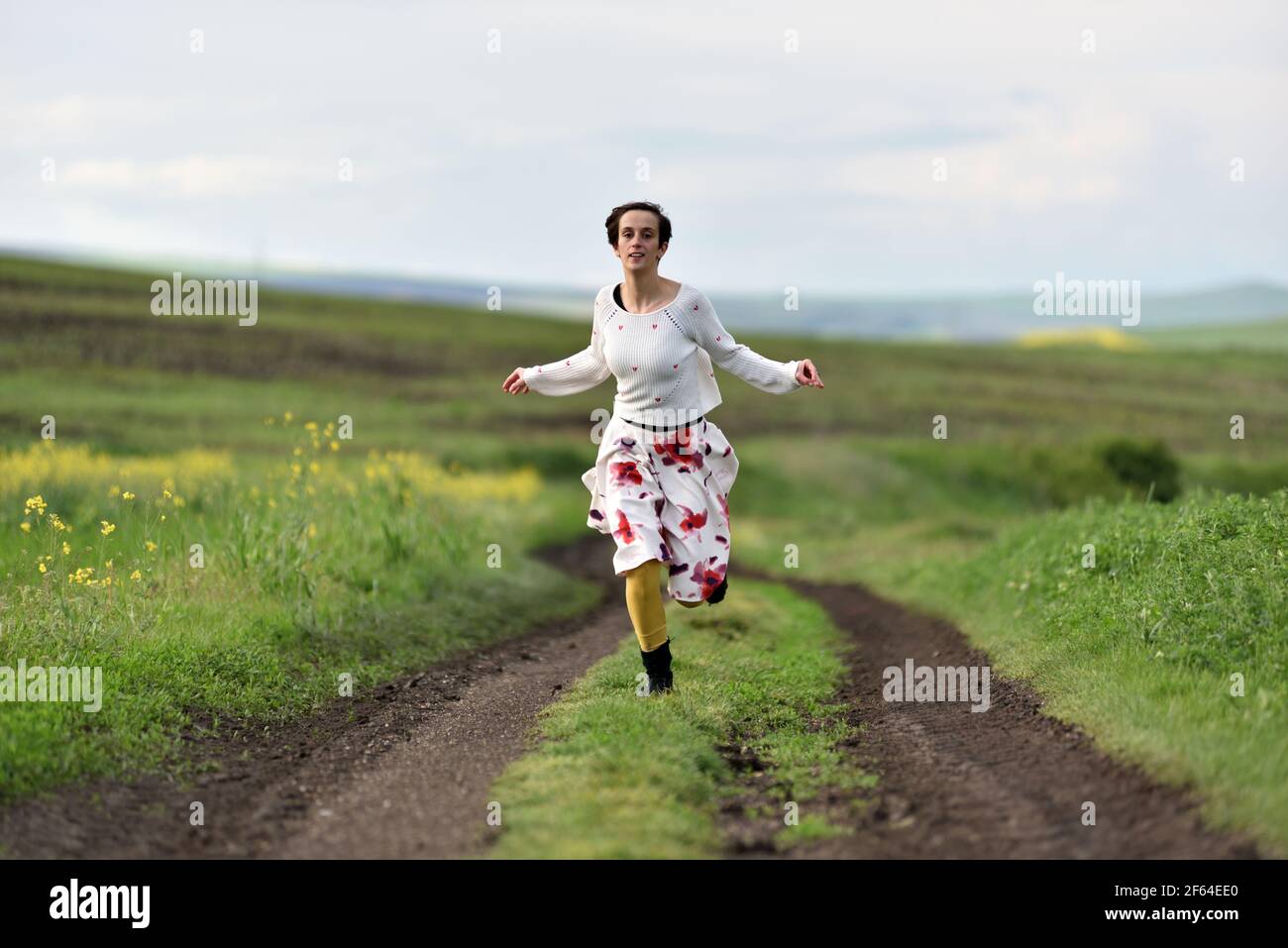 Joyful younf woman in skirt running in canola field in the spring Stock Photo
