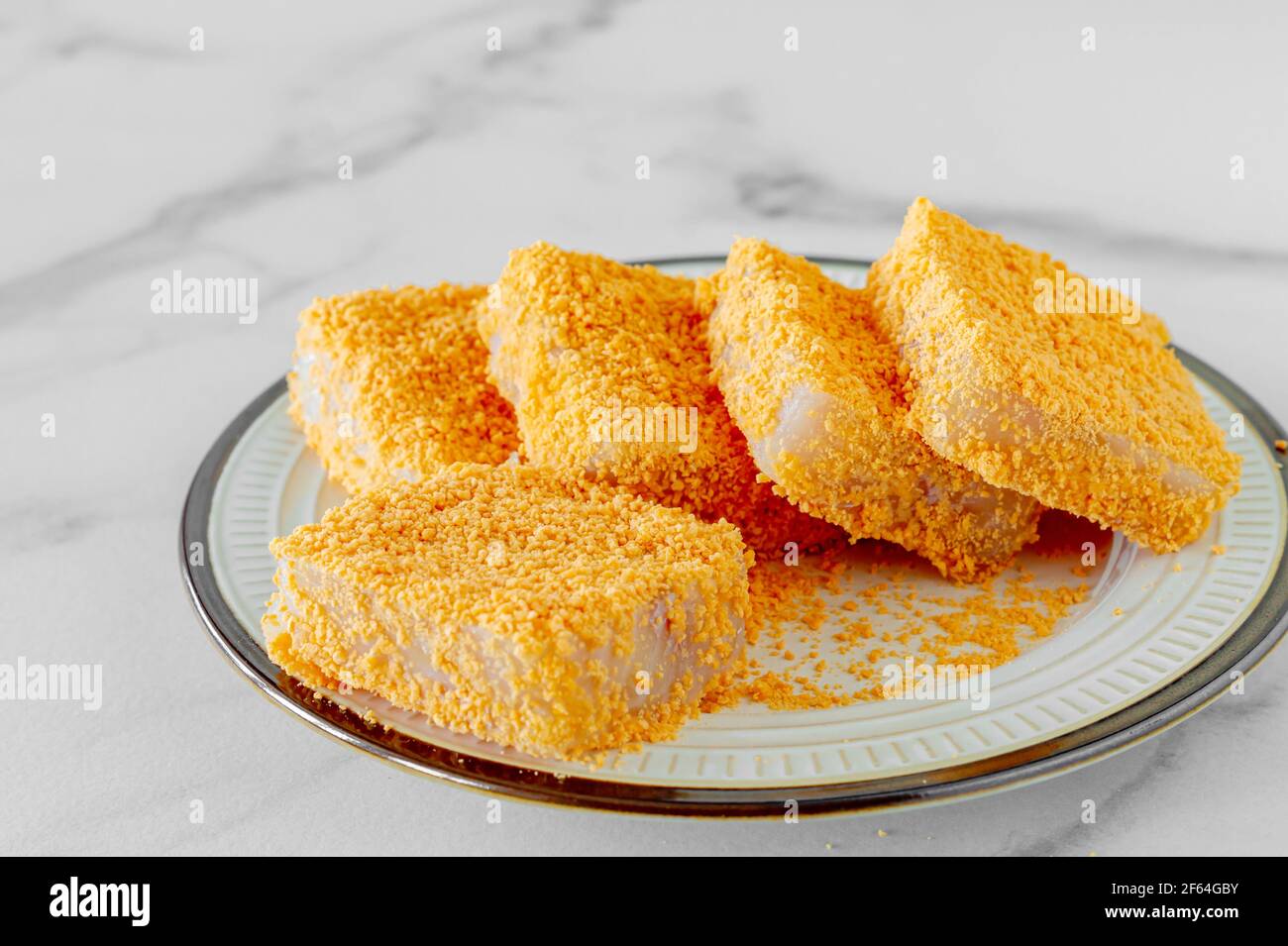 breaded fish patties on a plate prepared to cook. Stock Photo