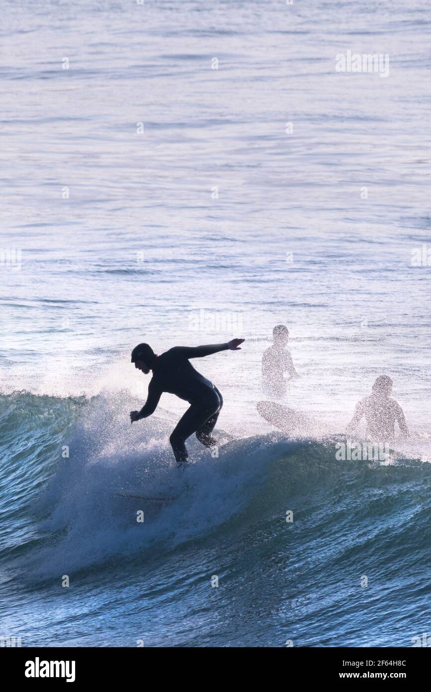 The silhouette of a surfer riding the crest of a wave at Fistral in ...