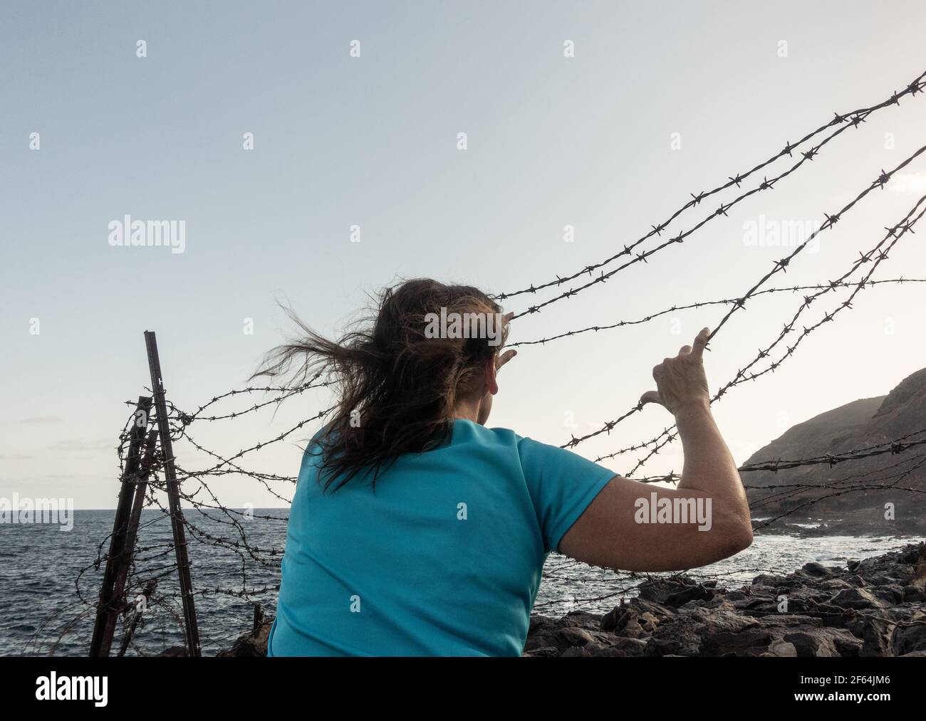 Woman behind coastal barbed wire fence: asylum, Brexit, illegal immigrant, human trafficking, slavery, domestic violence..., concept Stock Photo