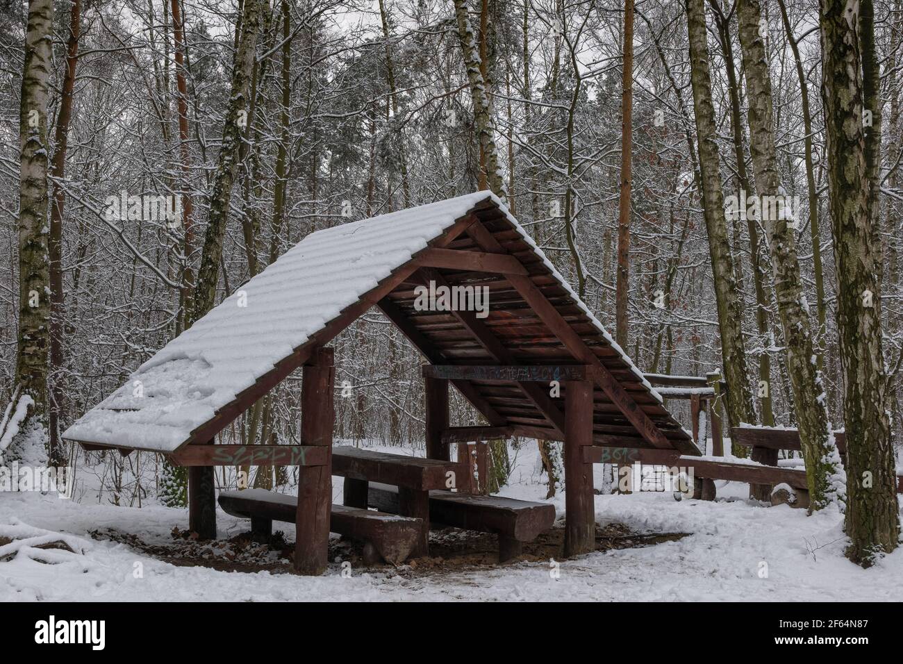 Rest area in winter forest for tourists, travellers, wooden shelter with bench, table and snow covered roof Stock Photo