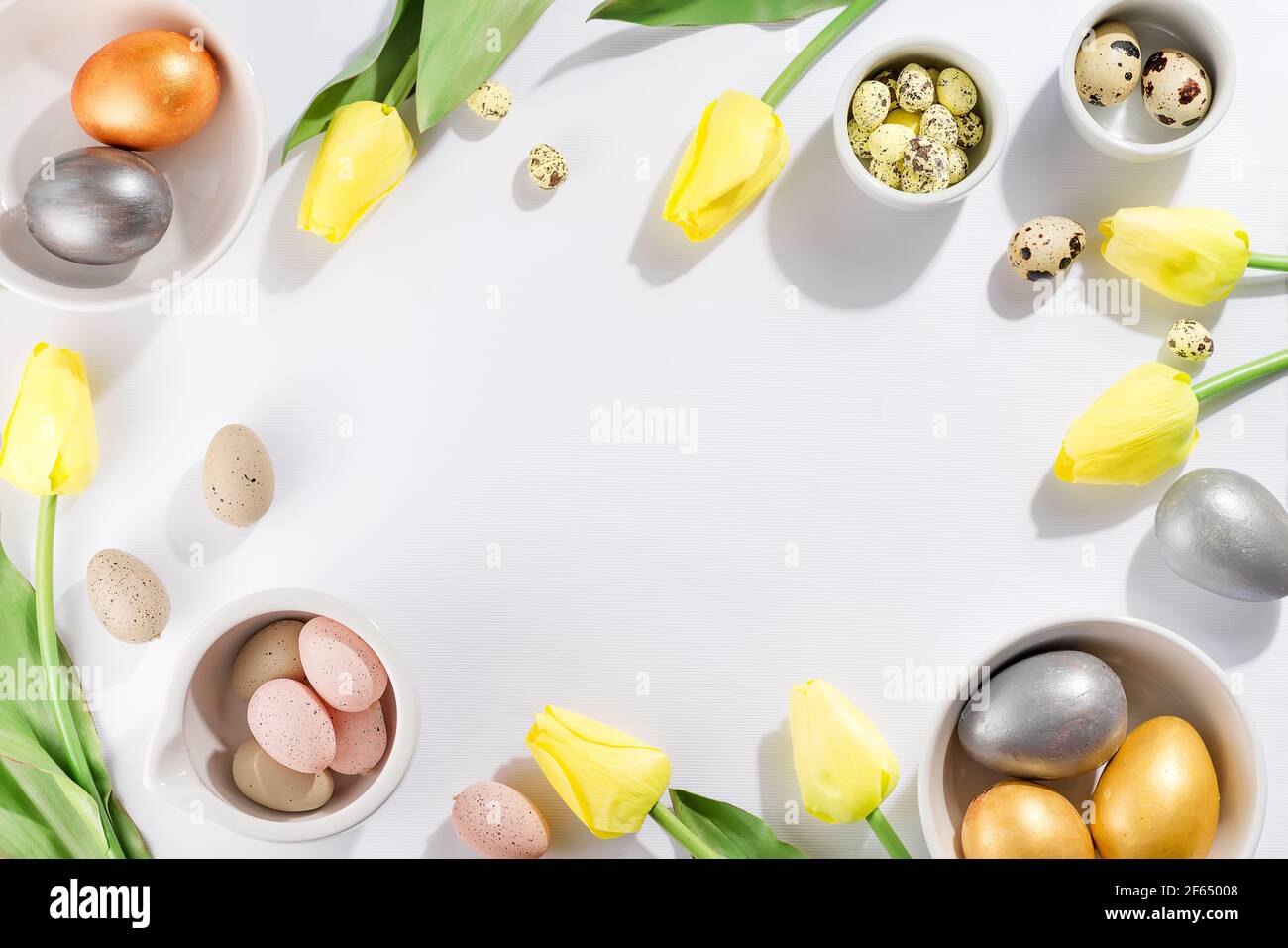 Colorful easter and quail eggs in bowl and tulips on white background ...
