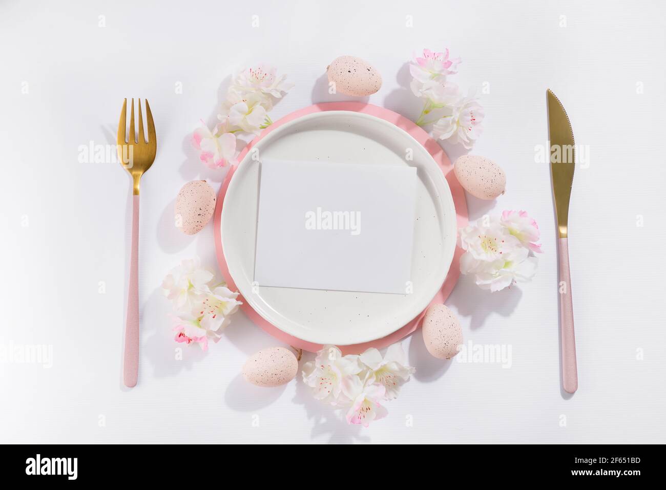 Easter table place setting with eggs, plate, cutlery and beautiful flowers, top view composing with card Stock Photo