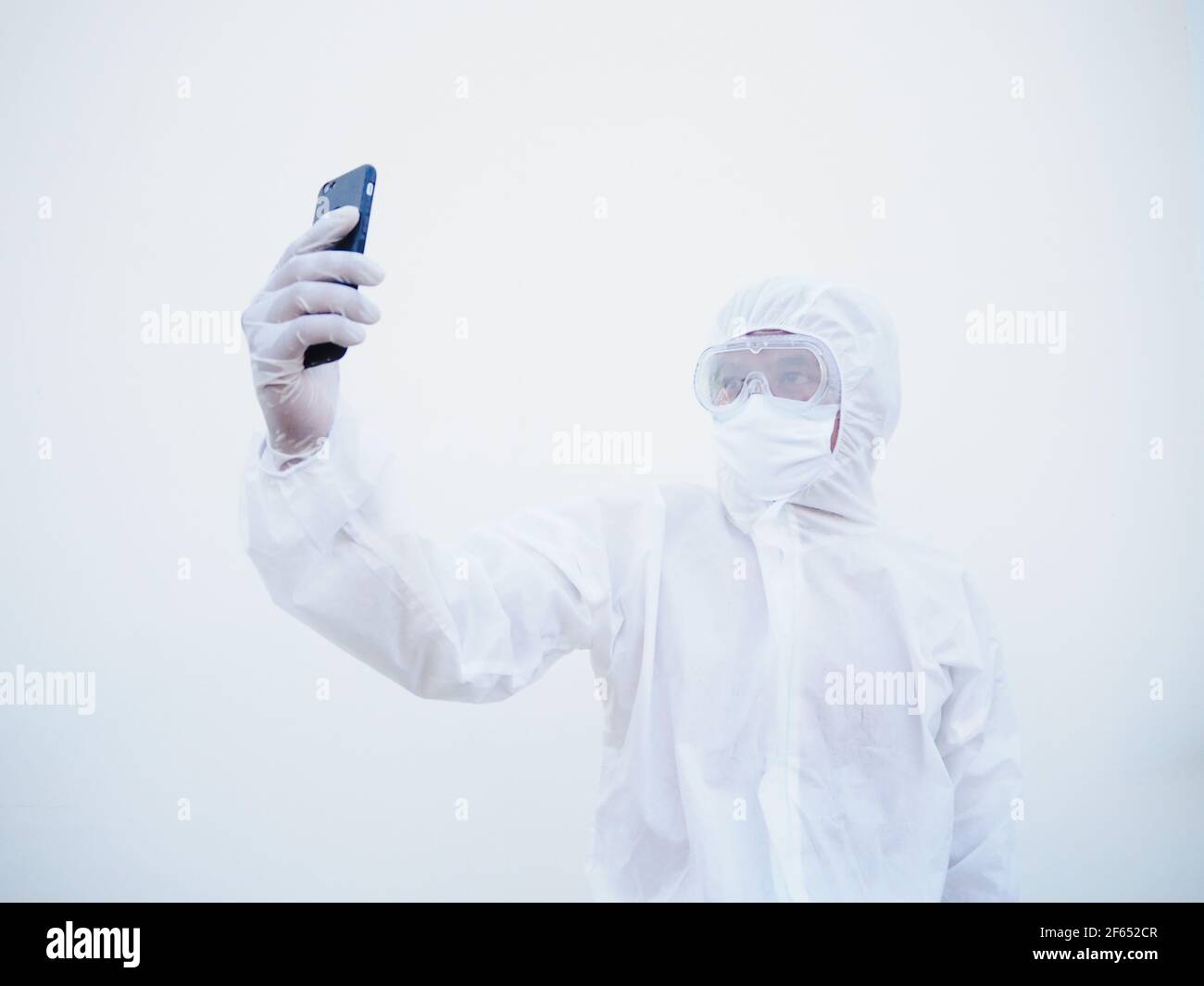 Young doctor or scientist in PPE suite uniform while using his phone for selfie and video chats with family or freind. coronavirus or COVID-19 concept Stock Photo