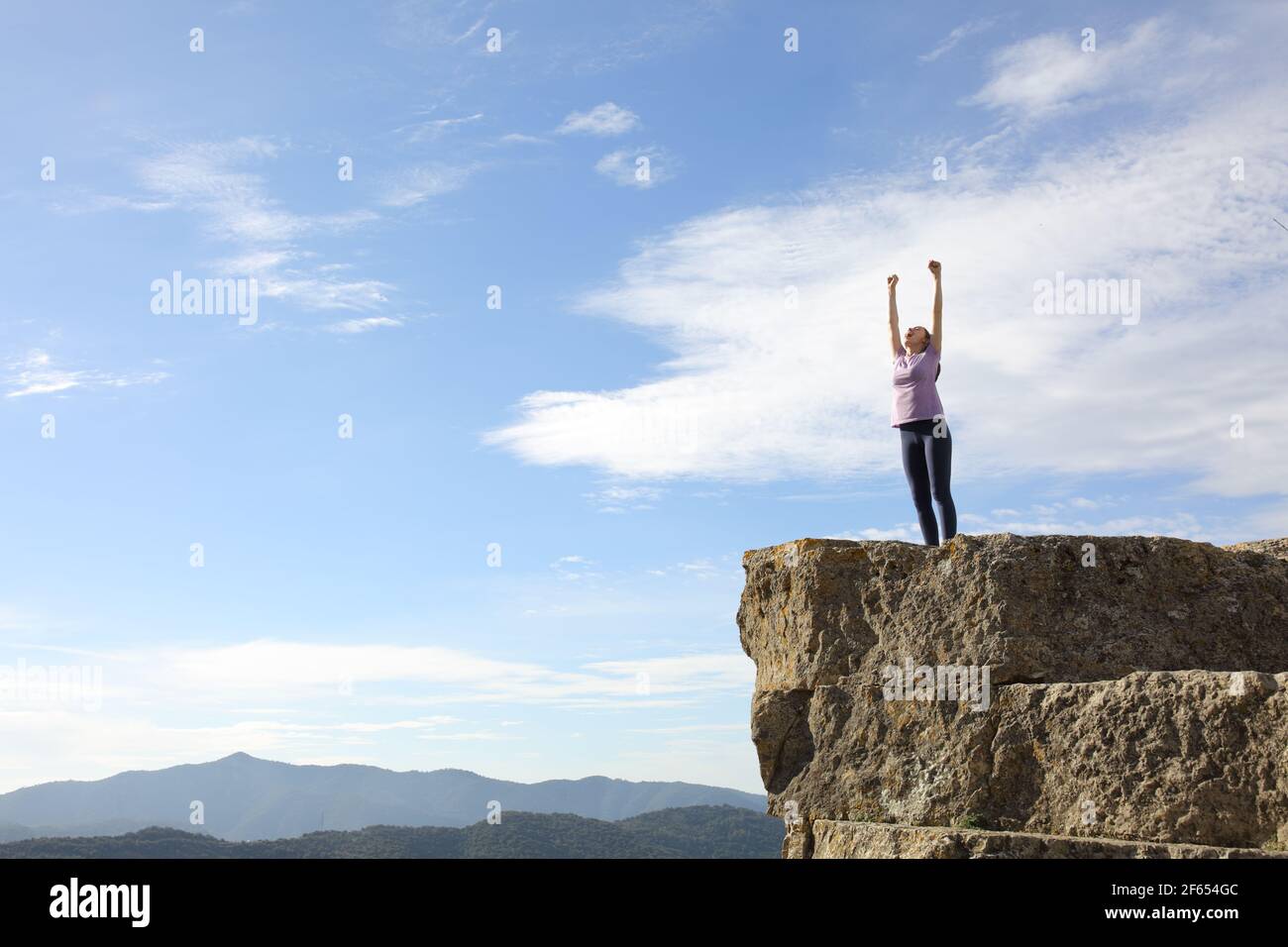 Excited runner raising arms celebrating success in the top of a cliff Stock Photo