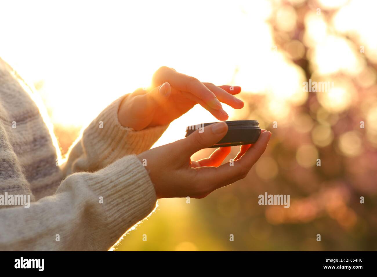 Close up of a woman hands applying moisturizer cream at sunset in a filed in spring Stock Photo