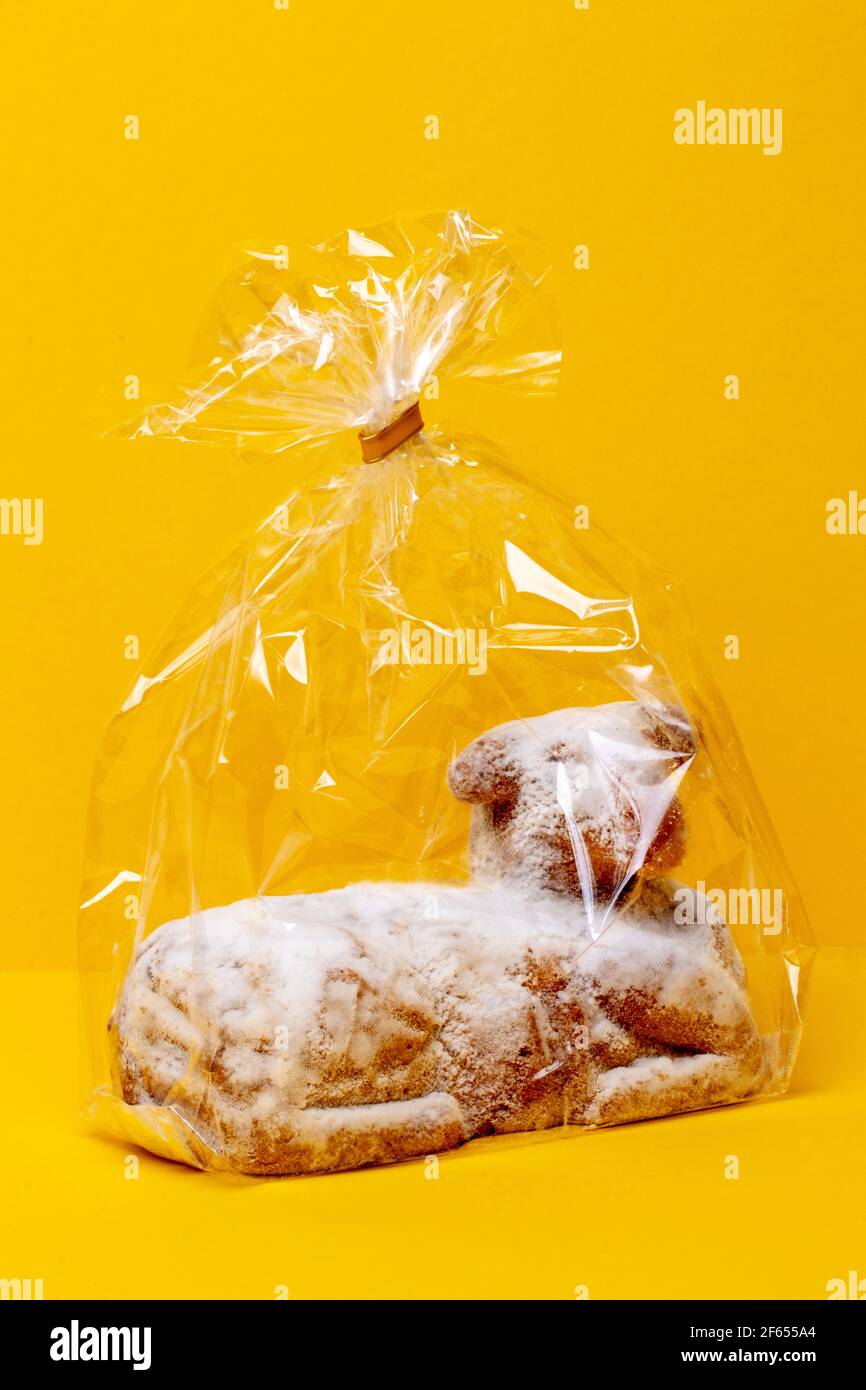Easter card template. Close-up of a traditional Easter lamb cake in a transparent wrapper on a yellow table and background. Copy space for design. Mac Stock Photo