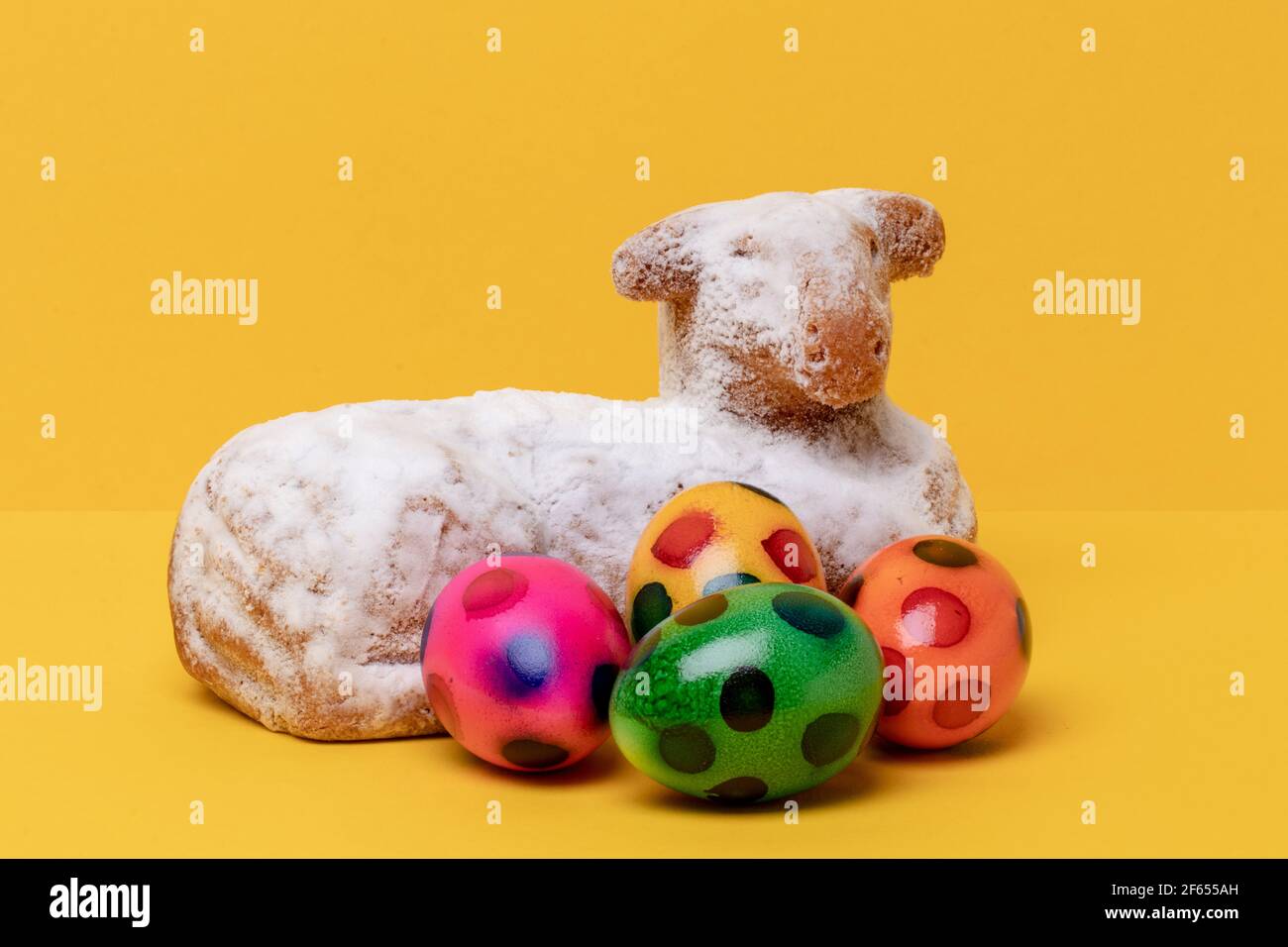 Easter card template. Close-up of a traditional easter lamb cake and some colorful eggs on yellow table and background. Copy space for design. Macro. Stock Photo