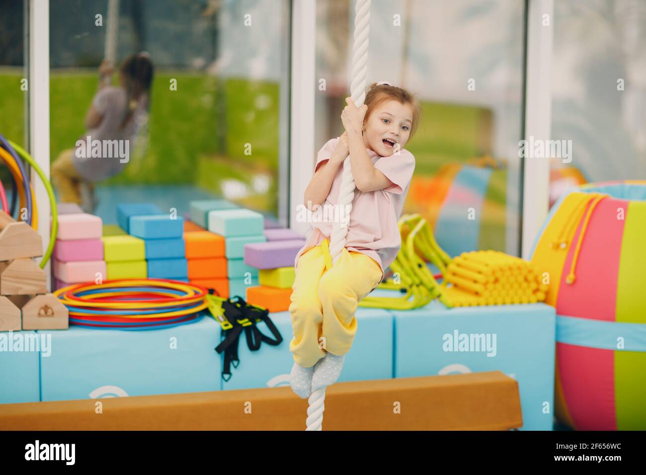 Kid girl doing exercises climbing tightrope in gym at kindergarten or