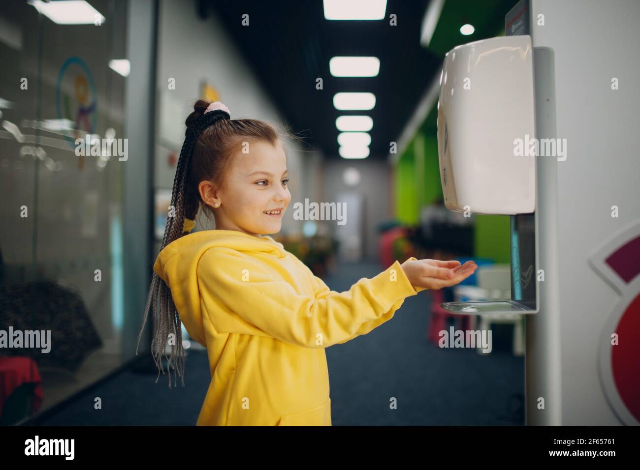 Child girl using automatic alcohol gel dispenser spraying on hands sanitizer machine antiseptic disinfectant, new normal life after Coronavirus COVID-19 pandemia. Stock Photo